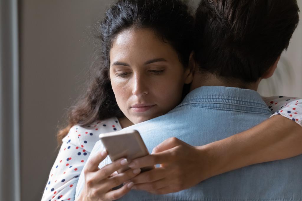 foto mujer abrazando a hombre mientras mira celular
